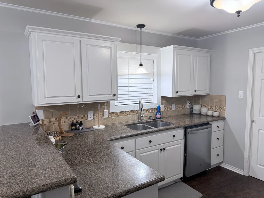 Kitchen cabinets painted white above speckled granite counters, with the original tile backsplash and pendant light