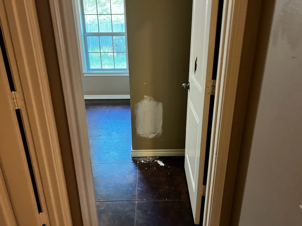 White joint compound drying on a patched wall, seen through an open door onto tile