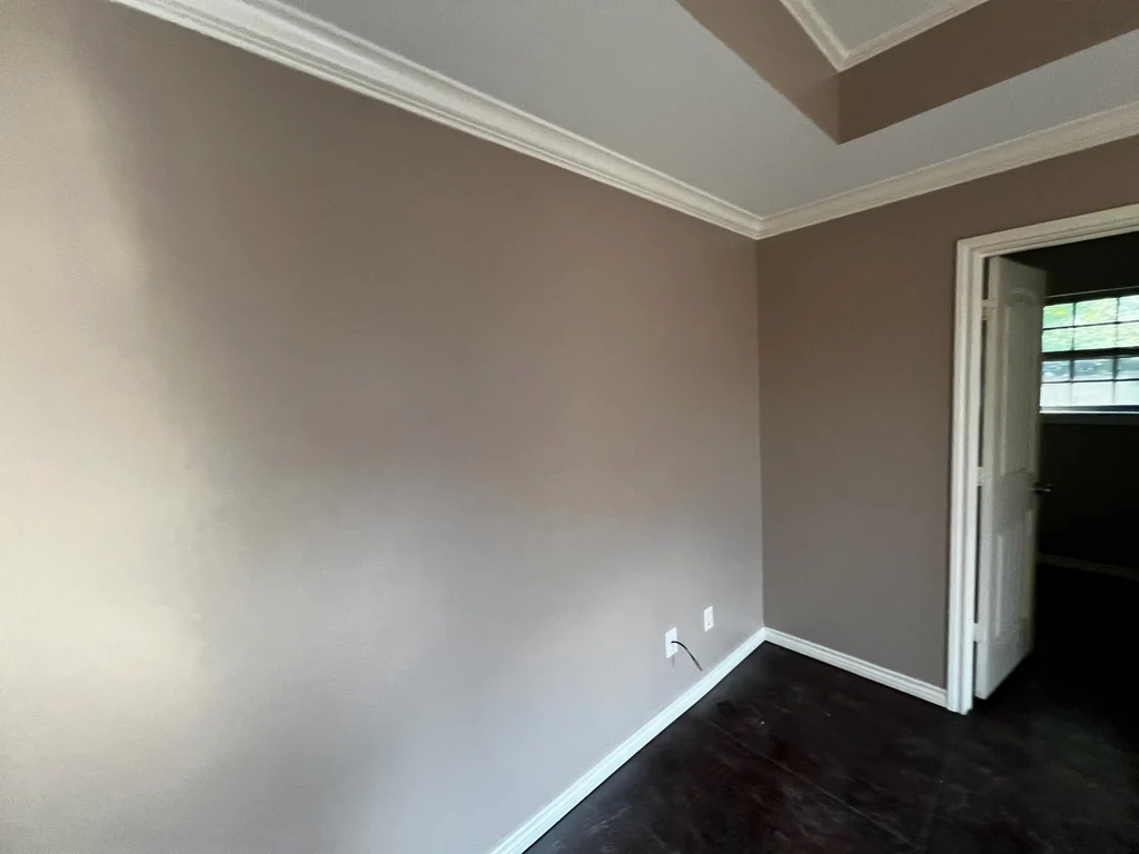 Bedroom repainted warm taupe with a tray ceiling, white crown molding and a doorway
