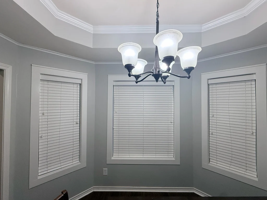 Dining room repainted gray with white trim, white blinds and a dark five arm chandelier