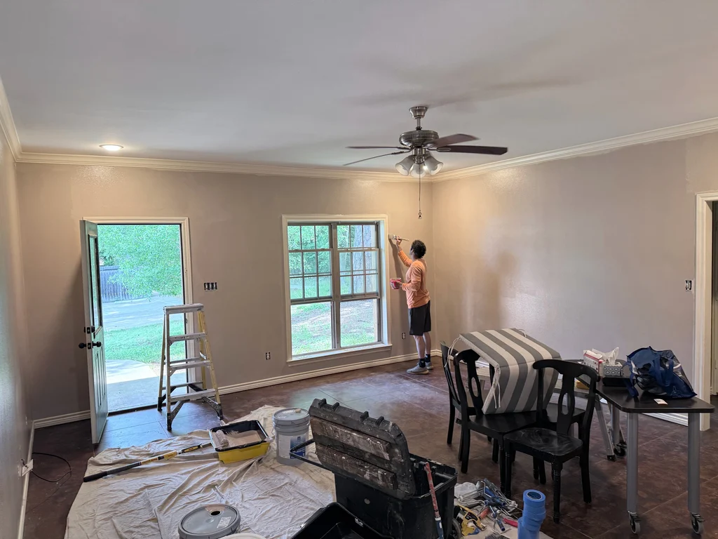 Painter cutting in along a window frame with a brush, drop cloths down and furniture covered