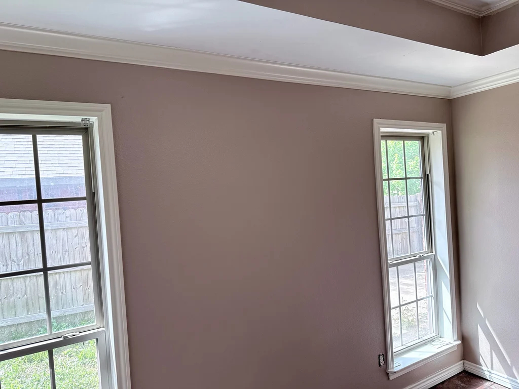 Room finished in soft mauve with white crown molding and two windows onto a fence