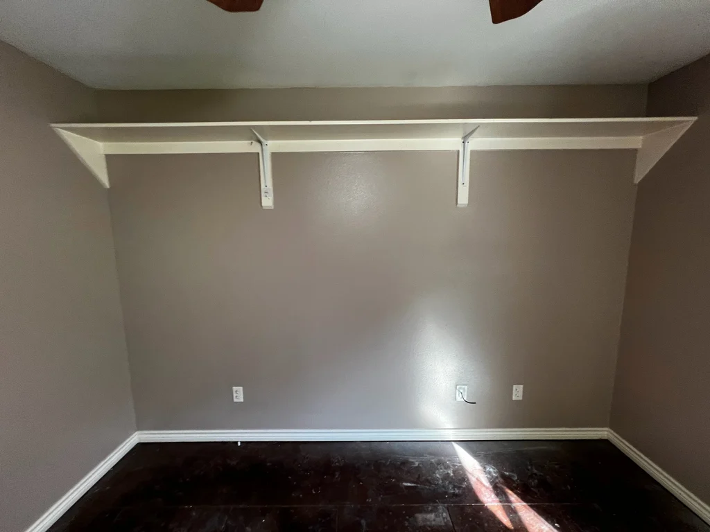 Finished room in taupe with a white painted shelf above dark tile flooring