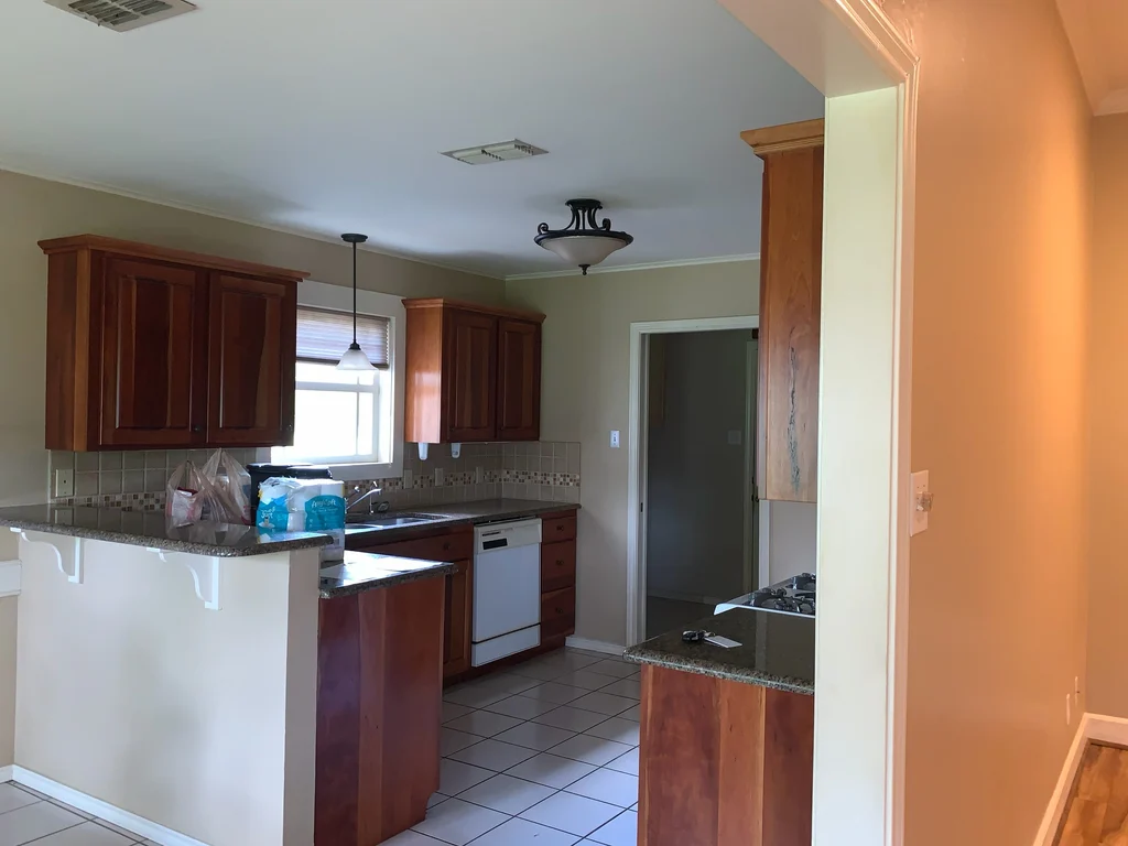 Before view of the same kitchen, dark stained cabinets and tan walls under a ceiling light