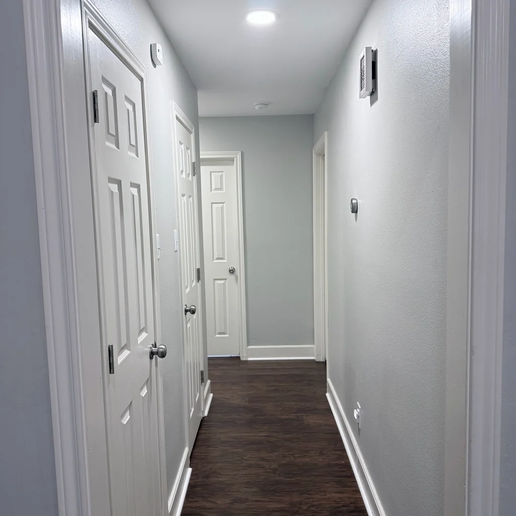 Matched after view of the same hallway, pale gray walls, white doors and a dark plank floor