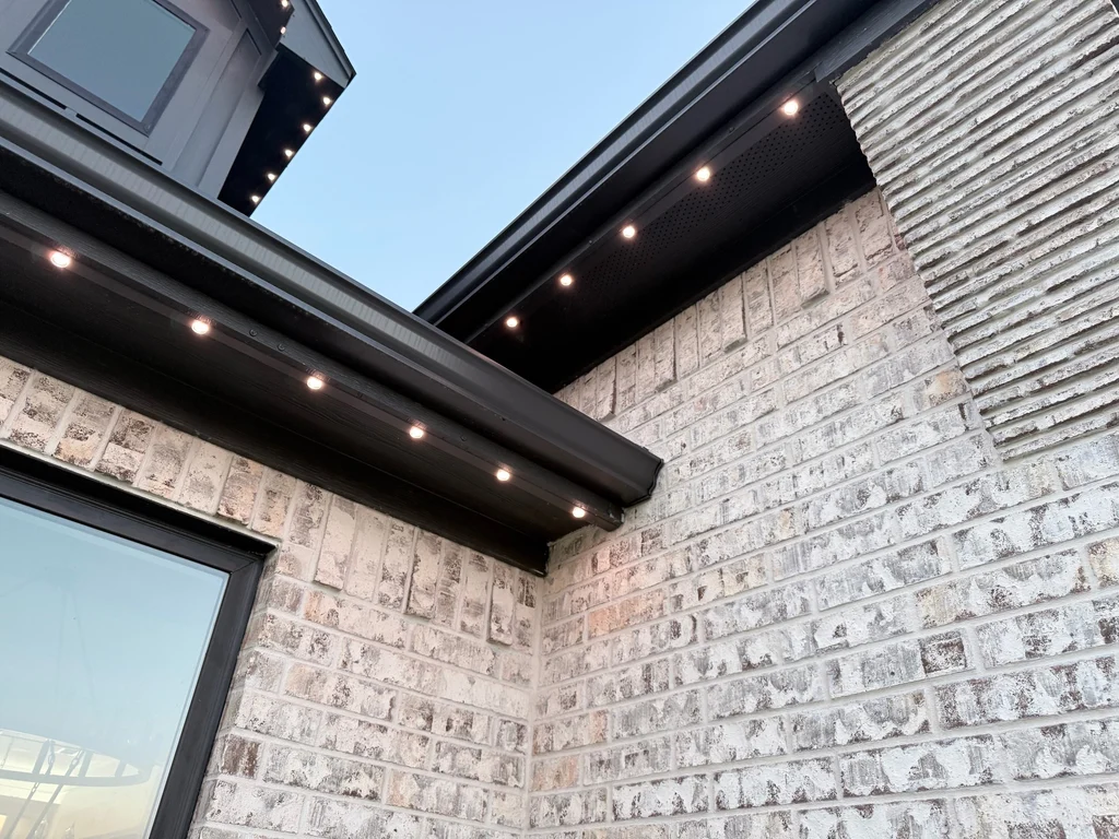 Warm white roofline lights seated in dark soffit track wrapping a corner of white brick