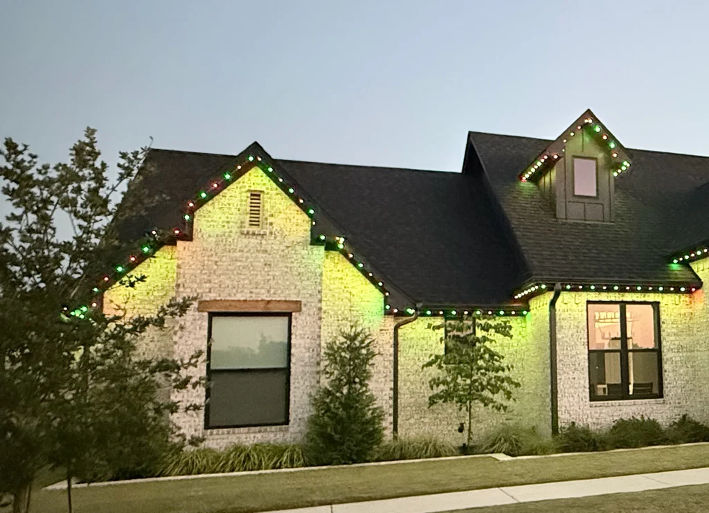 Two gables outlined in alternating red and green roofline lights at dusk on white brick