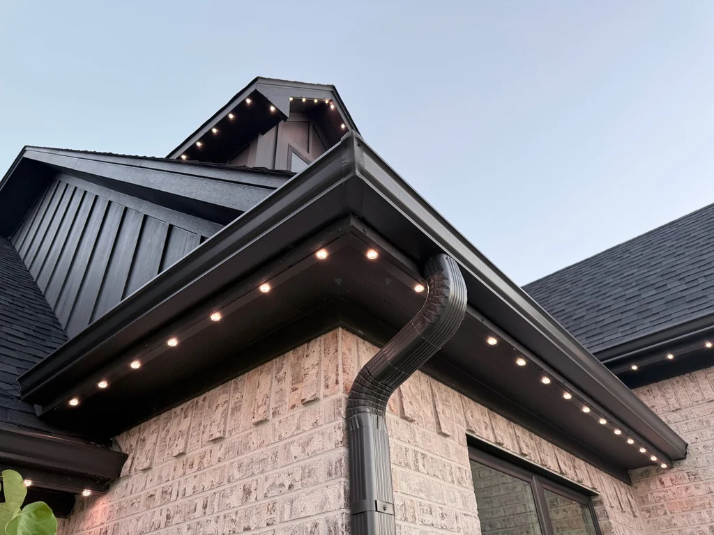 Warm white lights along a dark soffit and gable with standing seam metal roofing above
