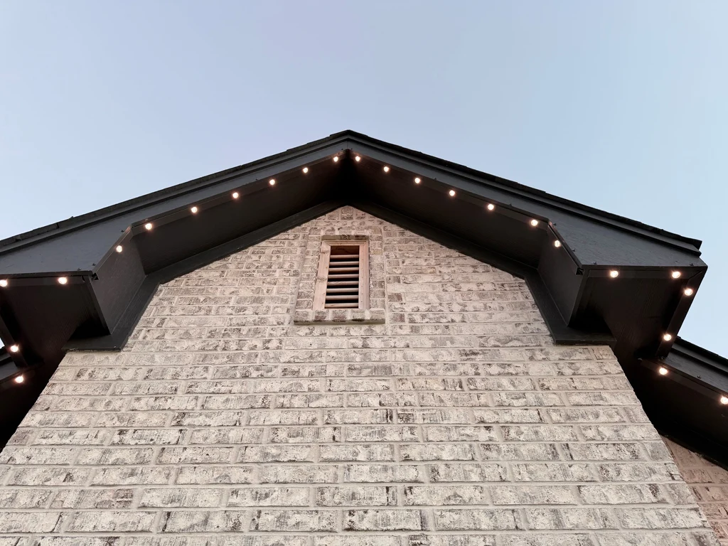 Warm white lights tracing both rakes of a brick gable peak with a louvred vent