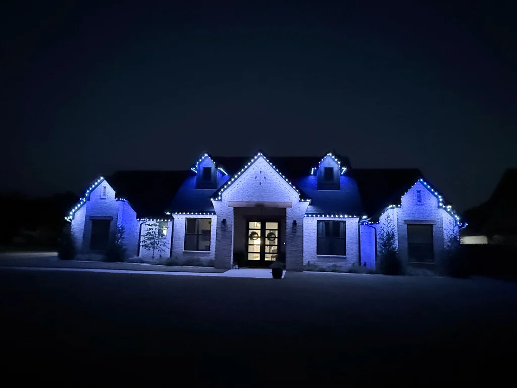 Single story brick home at night with every roofline and dormer outlined in blue