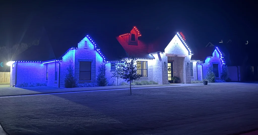 Brick home at night, rooflines in blue with one center gable picked out in red