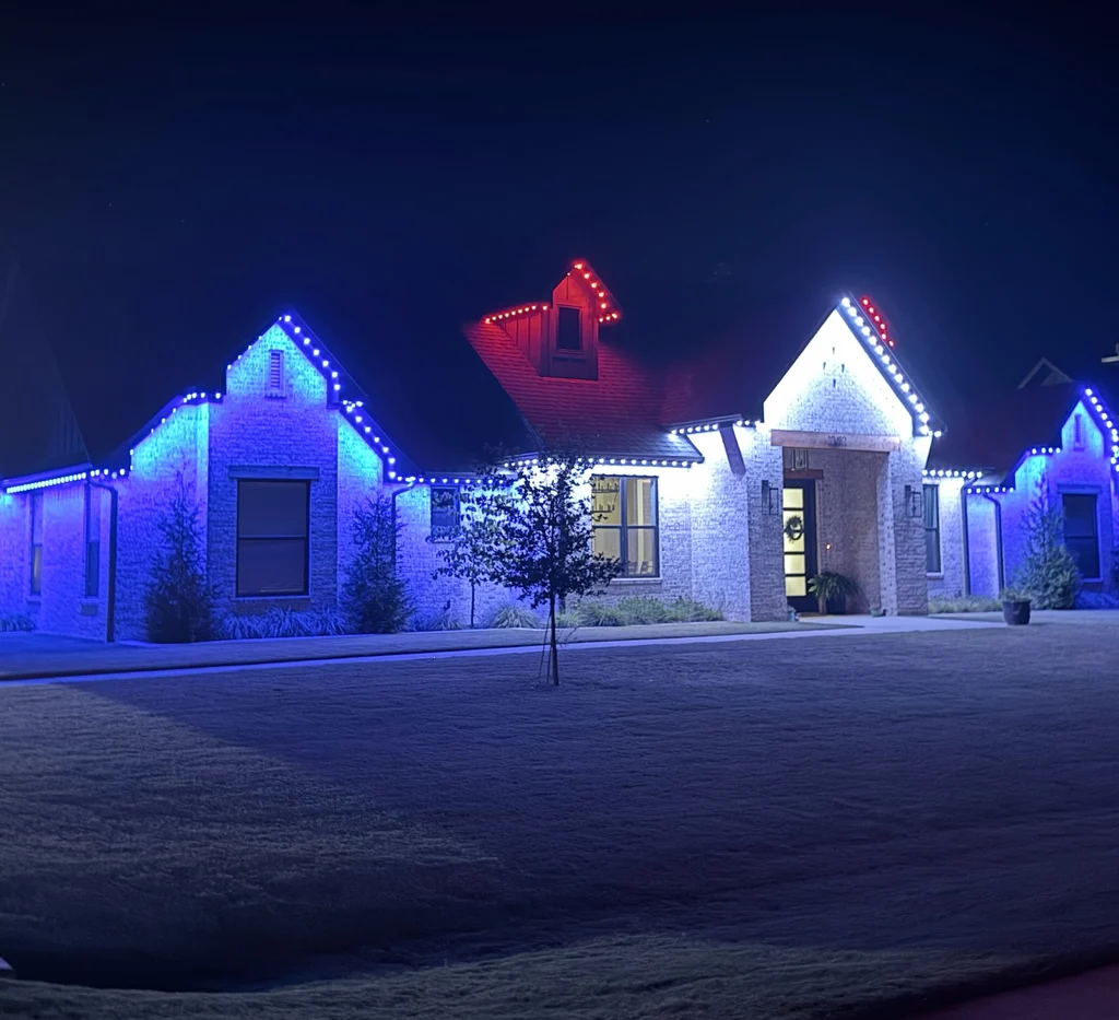 Upright night view of the same home, blue rooflines and a red gable above a dark lawn