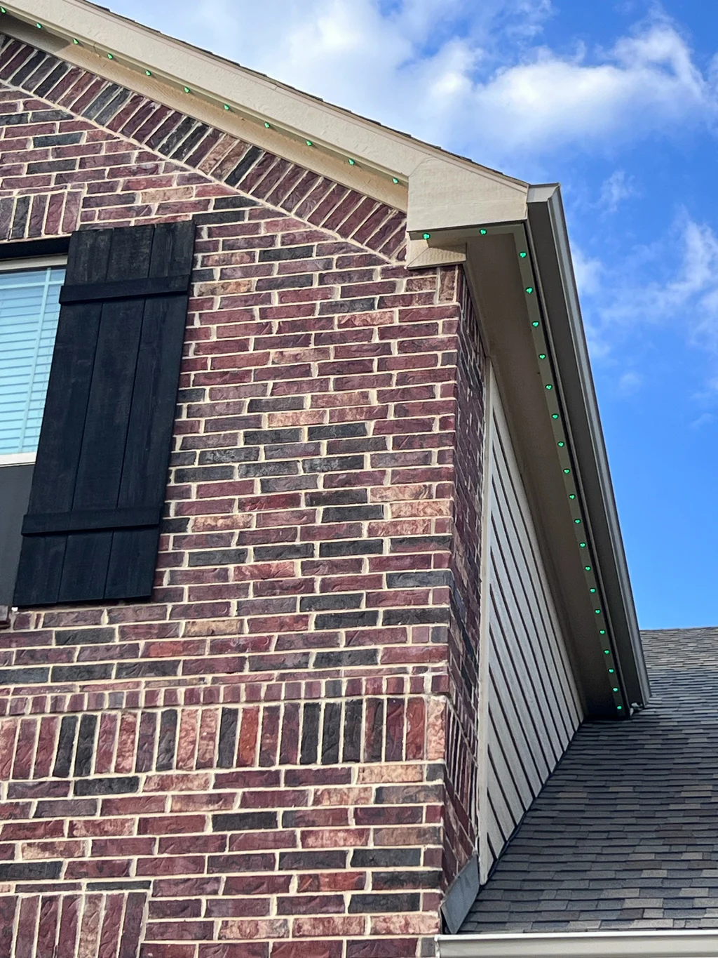 Lighting track in daylight along a gable rake where red brick meets pale siding